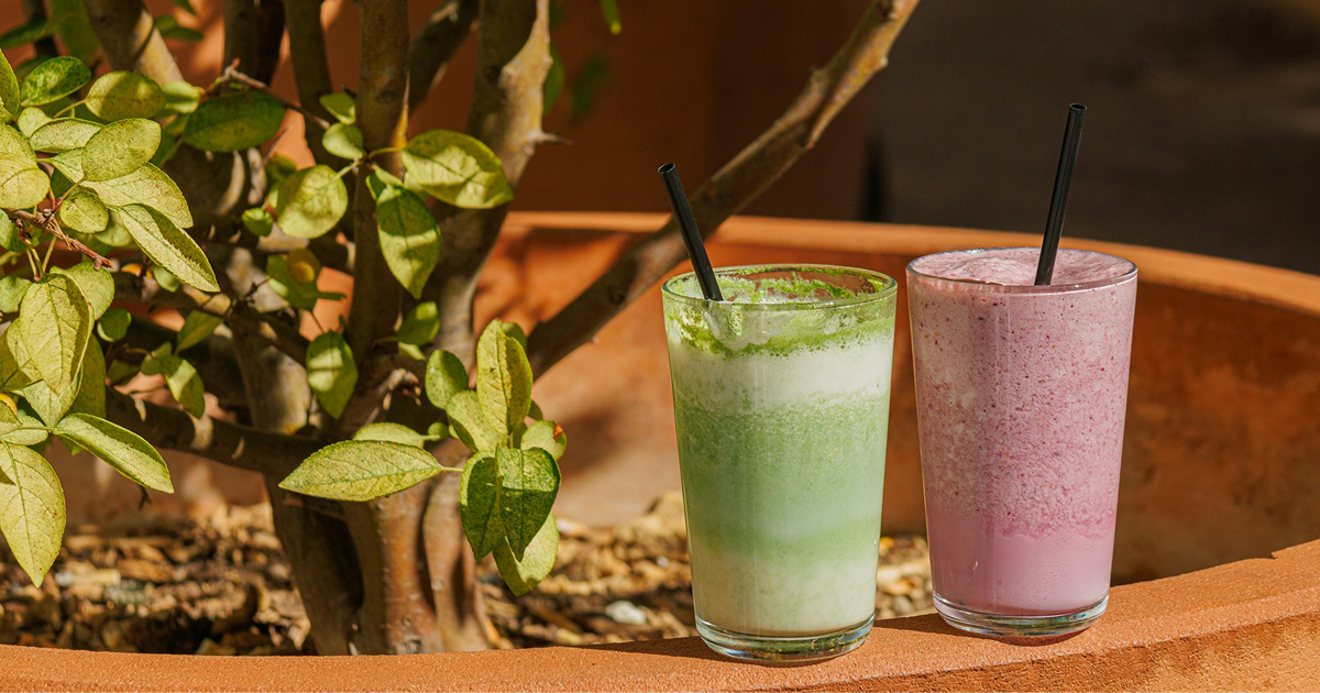 Two smoothies—green and pink—in tall glasses with black straws on a patio ledge.