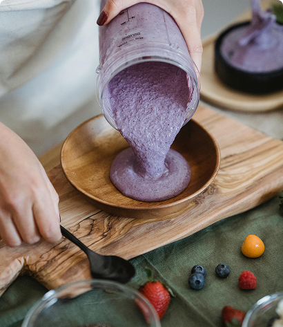 Pouring a purple smoothie from a blender cup into a wooden bowl.