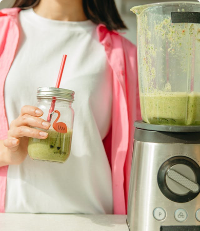 Woman holding a mason jar of green smoothie next to a countertop blender.