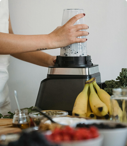Person using a personal blender surrounded by fruit and smoothie ingredients.