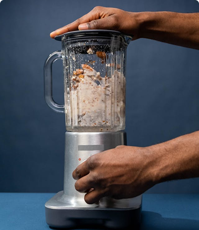 Hands operating a countertop blender with ingredients inside the jar.